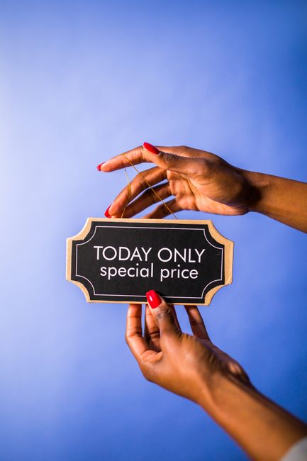 The image shows a close-up of a person's hands with red-painted nails holding a small rectangular sign with a black background and gold border, which displays the text 'TODAY ONLY special price'. The 